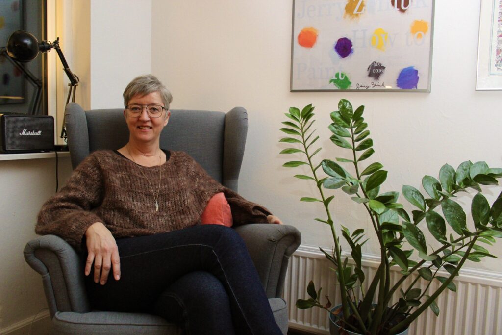 Kvinde sidder i stol med grøn plante ved siden af