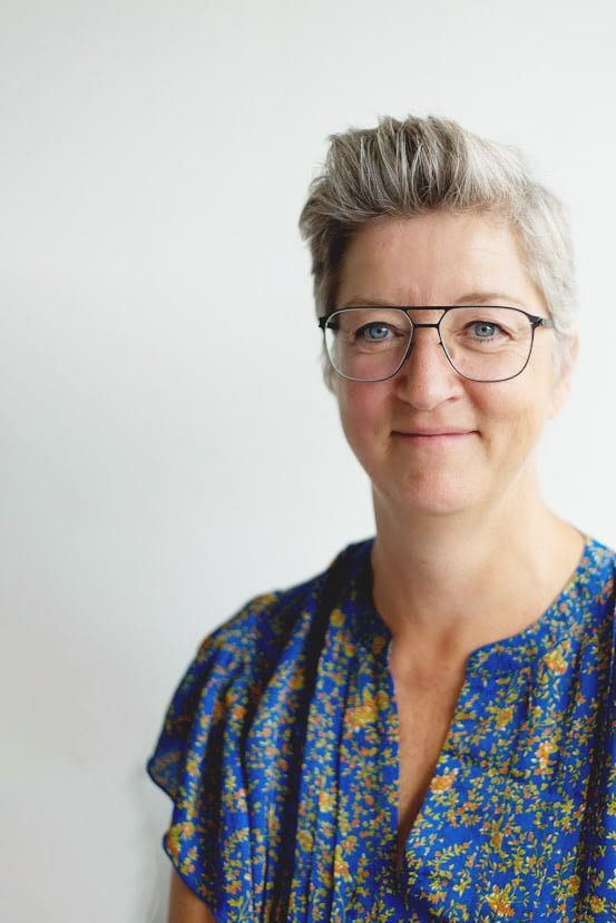 Smilende person med briller og blå blomstret skjorte